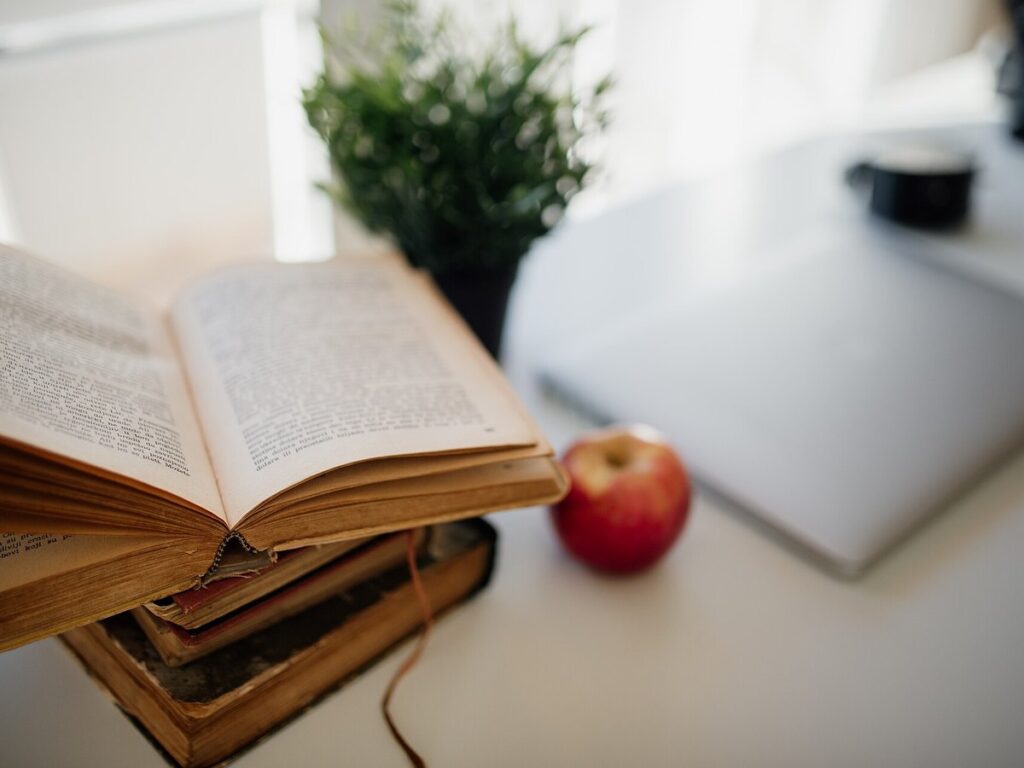 Cozy study space with an open book, fresh apple, and laptop on a desk in bright natural light