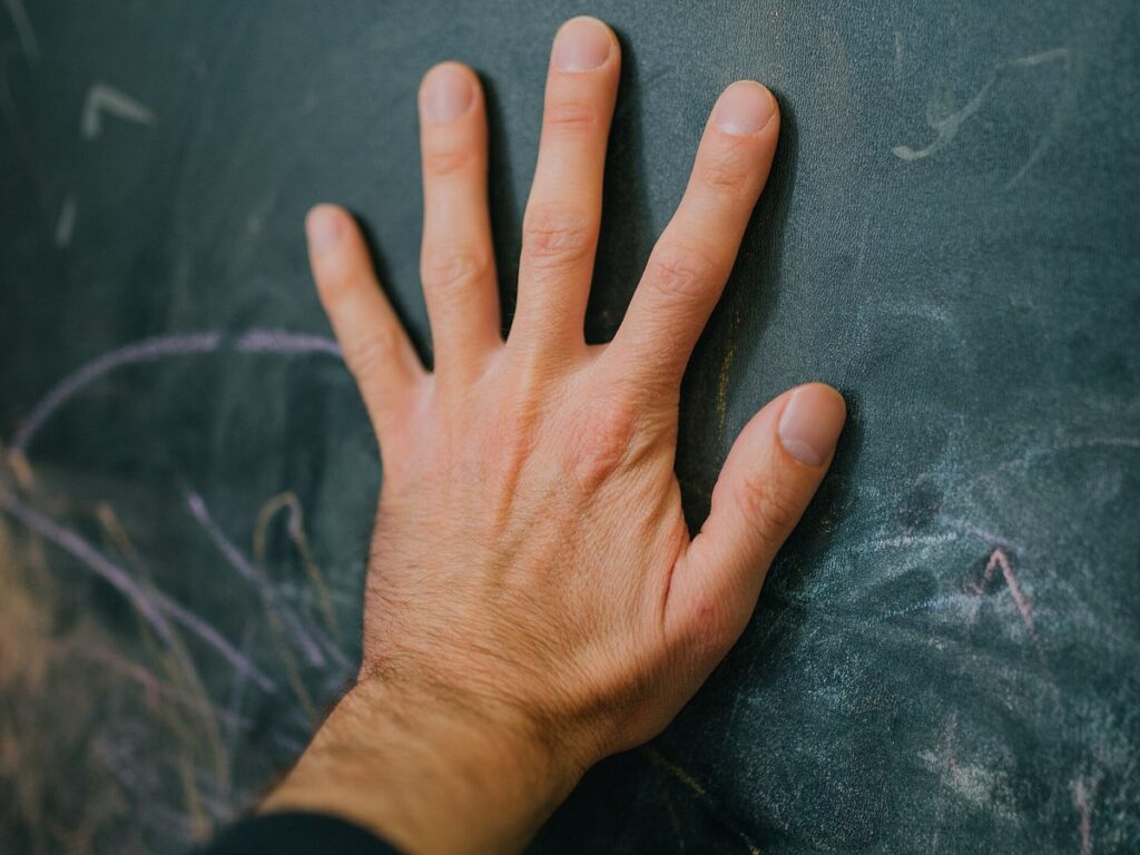 Hand pressed against a chalkboard revealing traces of past lessons and ideas in a classroom setting